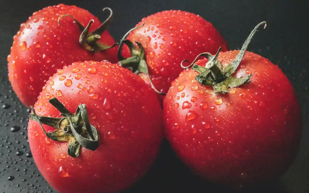 Fresh, ripe red tomatoes on a wooden surface, suitable for occasionally feeding to guinea pigs in moderation.